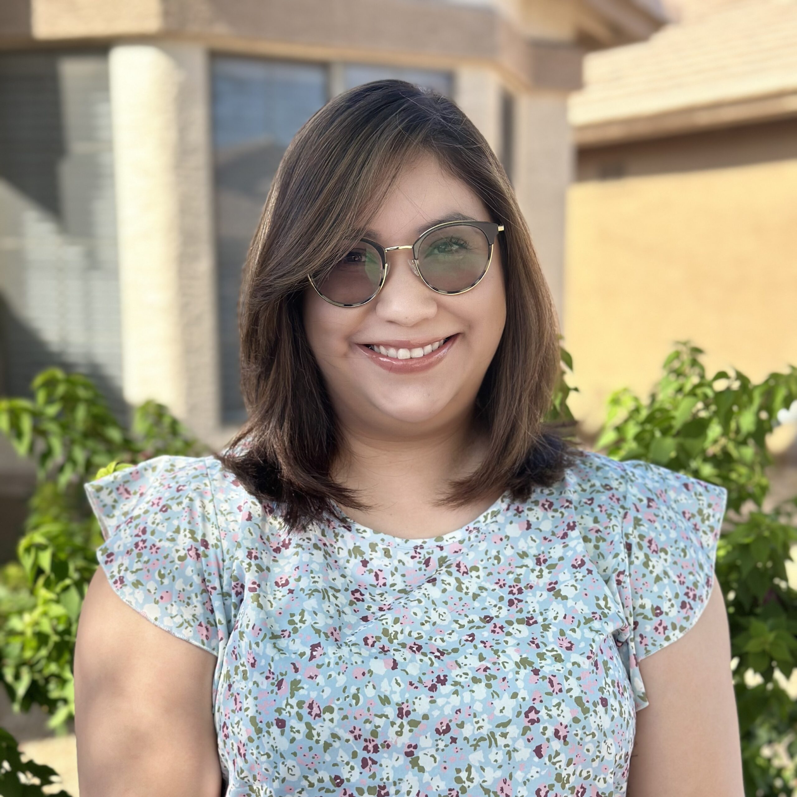 Smiling woman wearing sunglasses and floral dress.